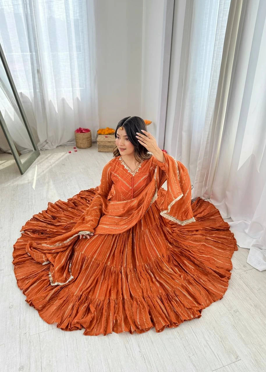 Woman in an orange saree sitting on a white floor with white curtains in the background